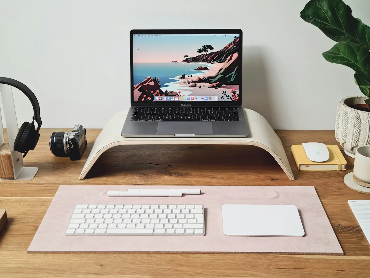 Laptop on a wooden stand at a tidy desk with a keyboard and trackpad